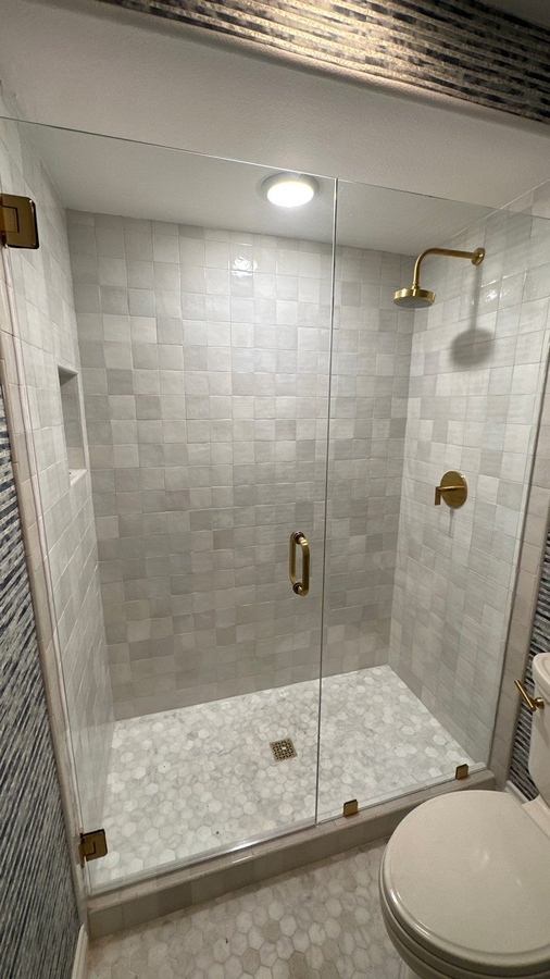 Frameless glass shower with white tile walls and gold har