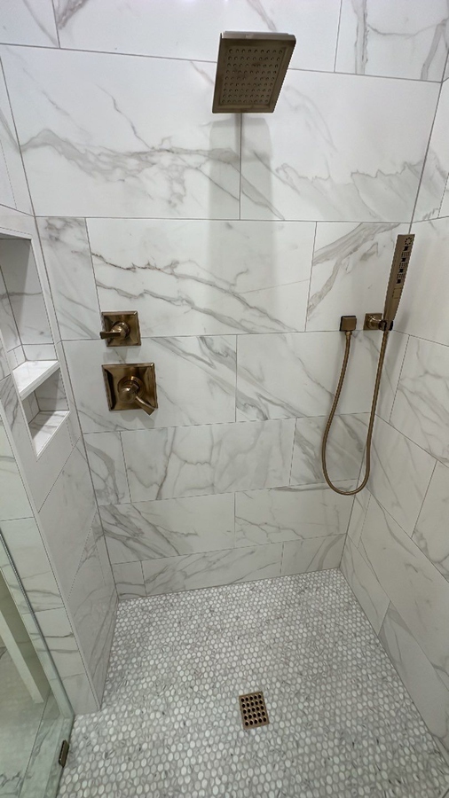 Close-up of marble shower wall with rain head and handheld spray in Alamo Heights remodel 