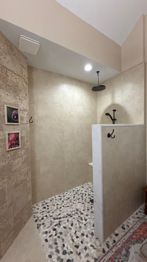 Open walk-in shower with pebble tile flooring and overhead rain shower insta