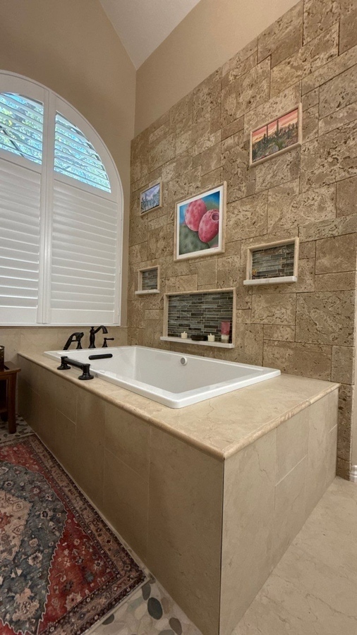 Stone tile accent wall and built-in shelves behind soaking tub in San Antoni