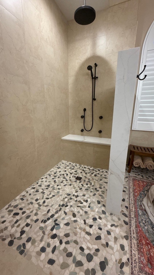 Walk-in stone-floor shower with black fixtures and bench installed by Wade C