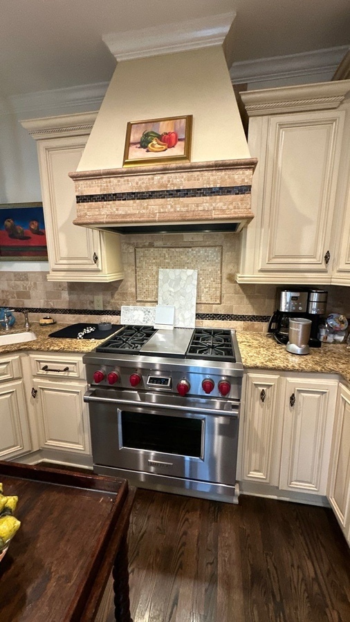 Custom tile backsplash and high-end range beneath decorative hood in San Antonio kitchen remod