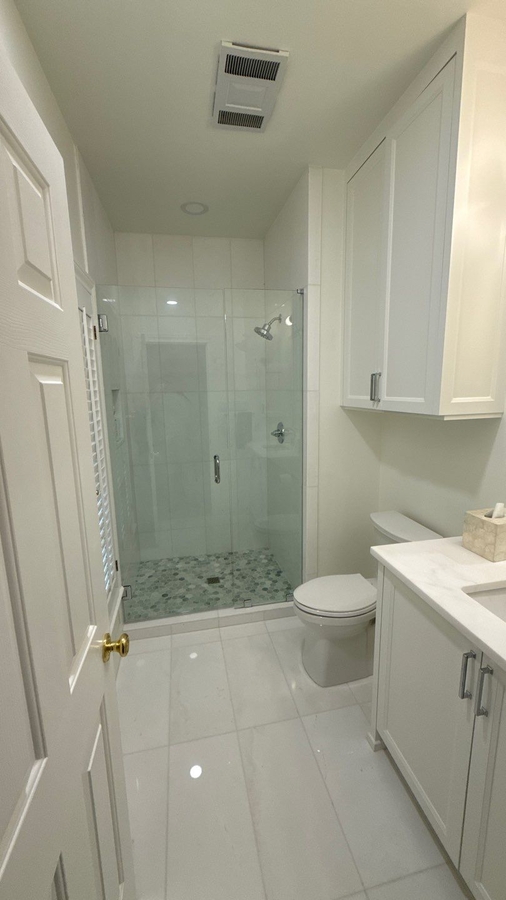 Modern white bathroom remodel with walk-in glass shower in San Antonio by Wade Caldwell