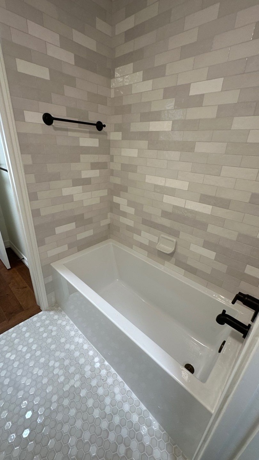 Updated bathtub alcove featuring soft neutral tones and modern matte black fixtures by Wade Cal