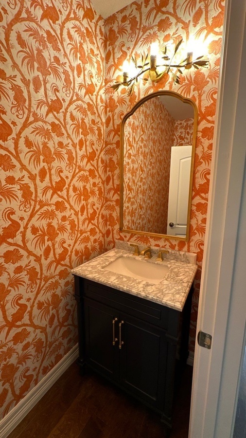 Vibrant powder room with orange botanical wallpaper and gold mirror in Olmos Park, TX by Wade C